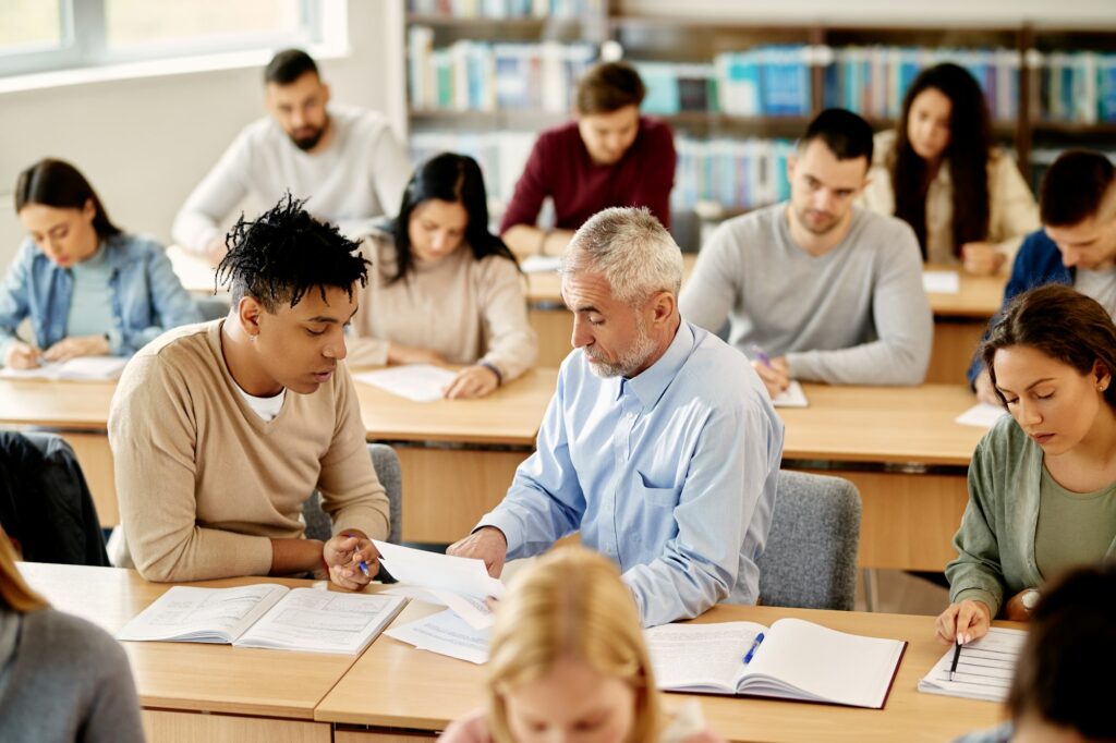 Mature teacher talking to his student while assisting him with the lecture in the classroom.